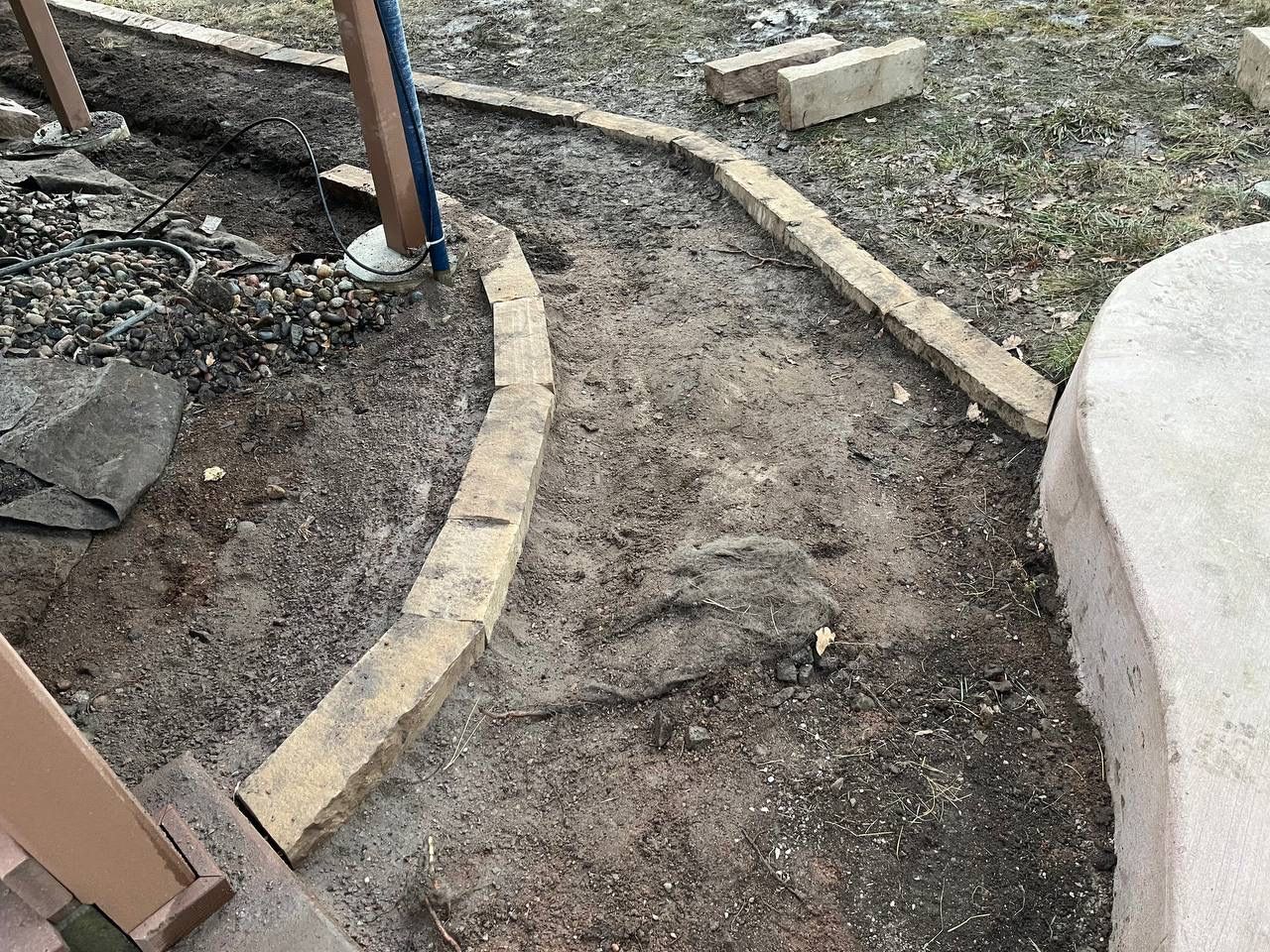 Curved dirt garden path bordered by stones and bare ground near a white structure