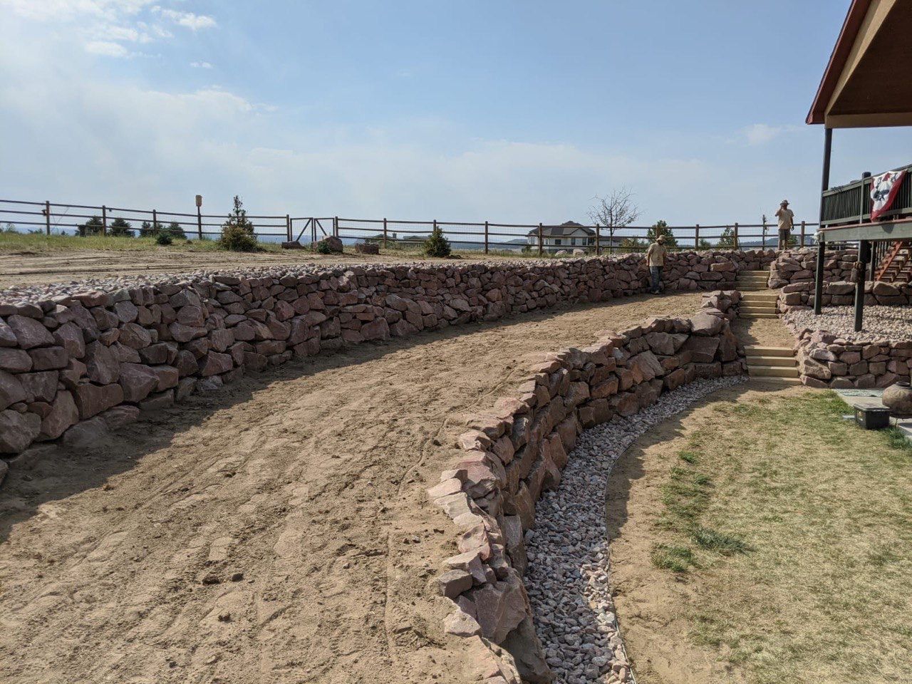 A stone wall surrounds a dirt field in front of a house