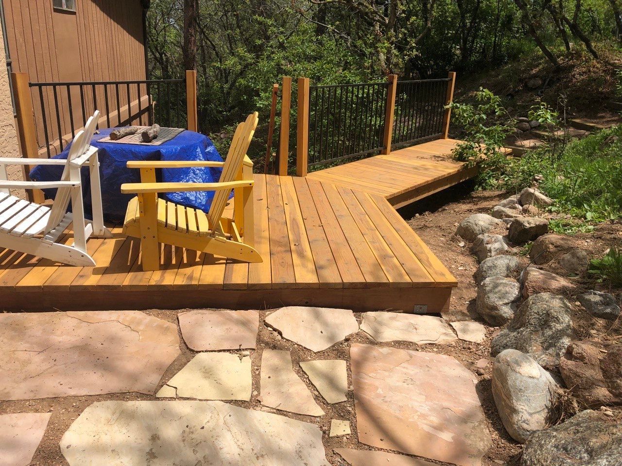 Wooden patio with yellow and blue chairs beside a stone path and rocky garden stream