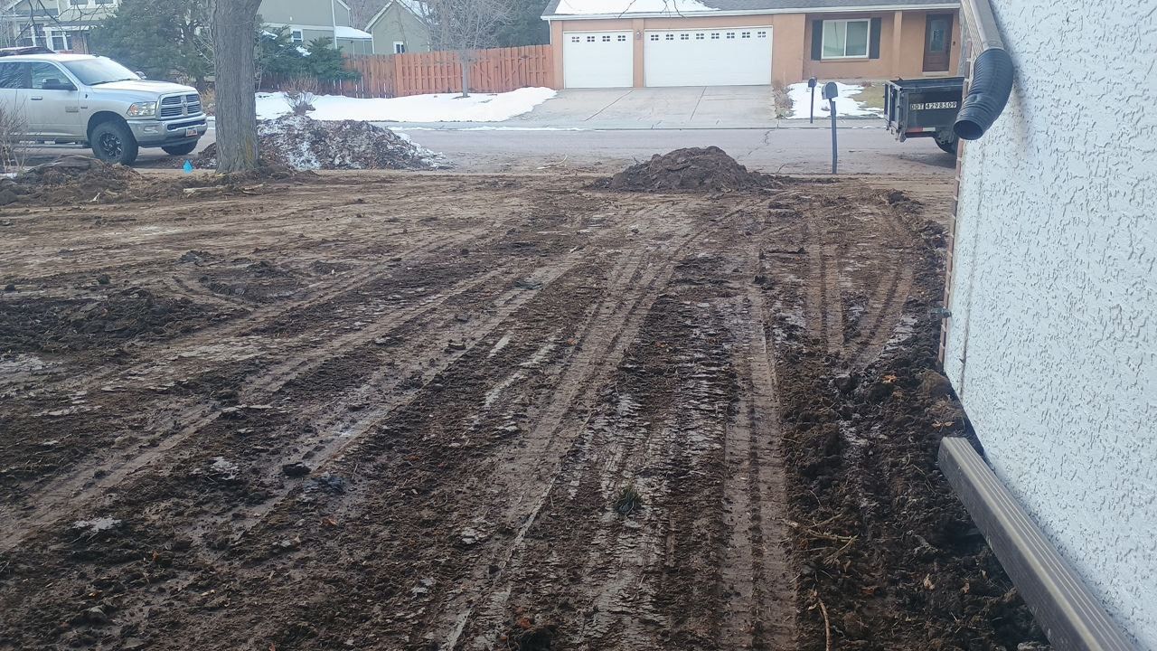 Muddy driveway and snowy yard in front of a suburban house on a winter day