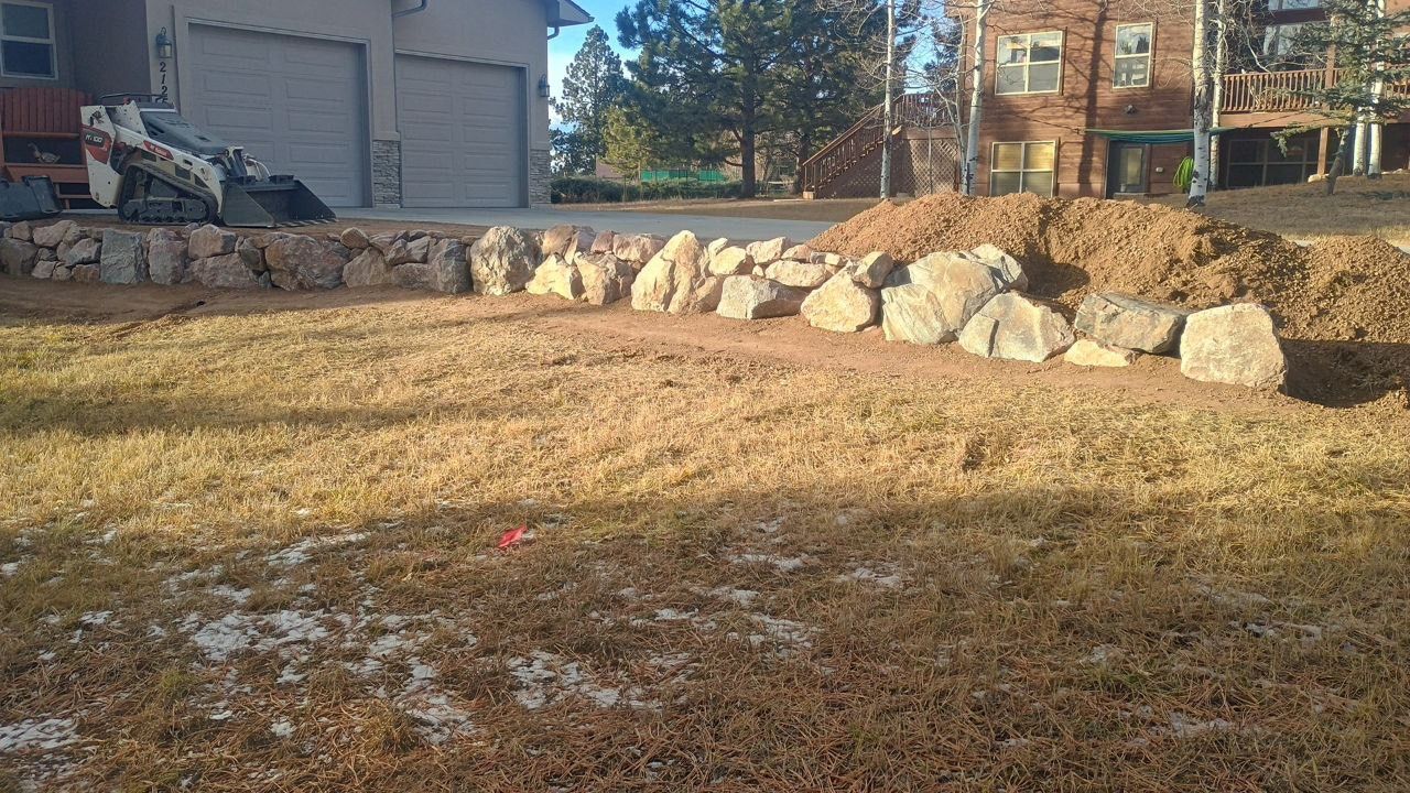 Rock retaining wall along a grassy yard beside a house on a sunny day