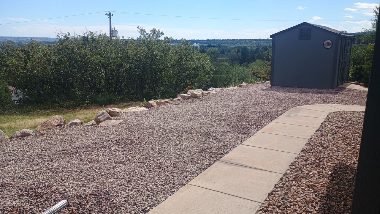 Gravel path leading to a small gray shed beside desert shrubs under a clear blue sky