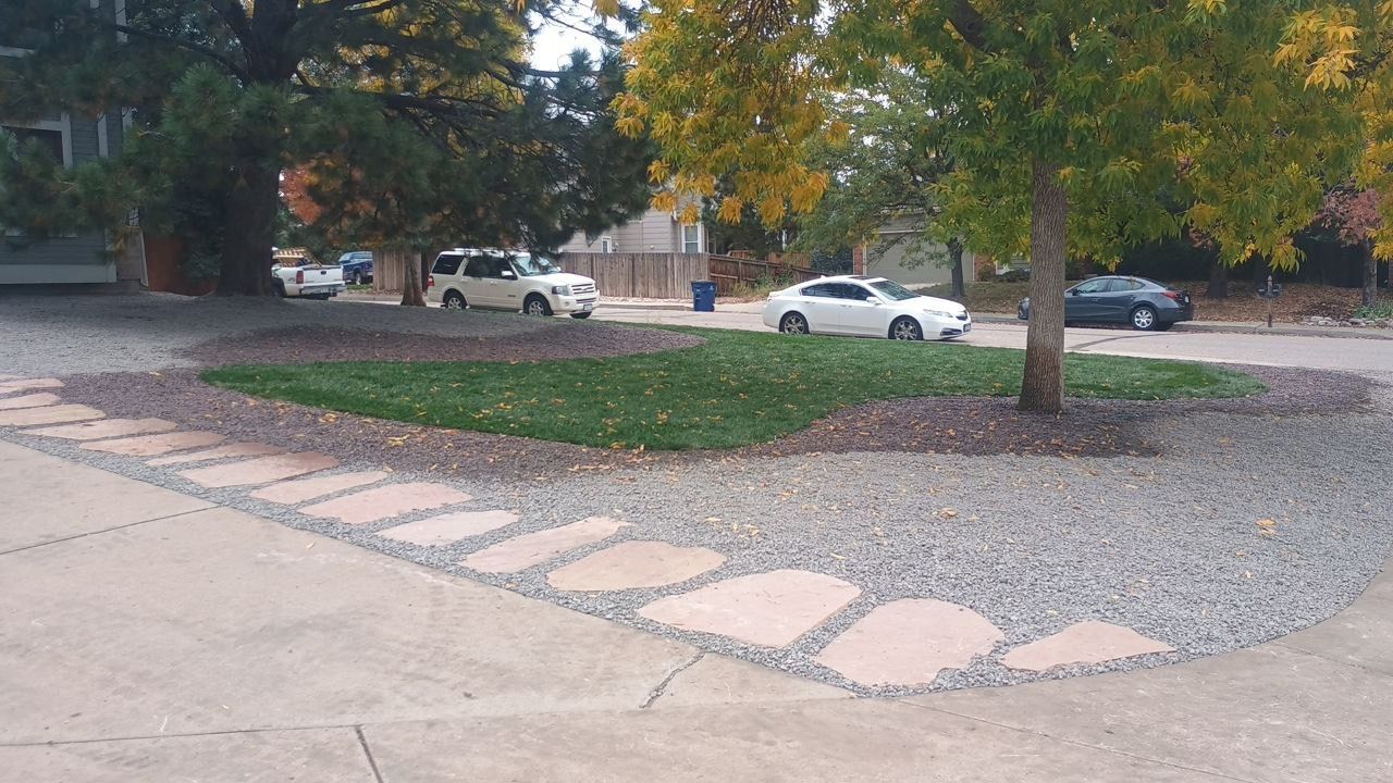Landscaped parking island with a tree, gravel, and stone edging beside a street with parked cars