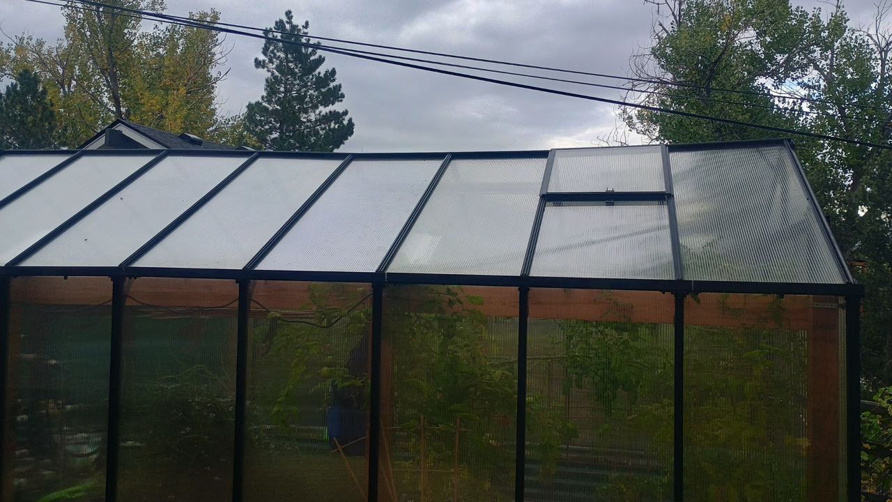 Glass greenhouse with a slanted roof and tall windows in a garden under cloudy sky