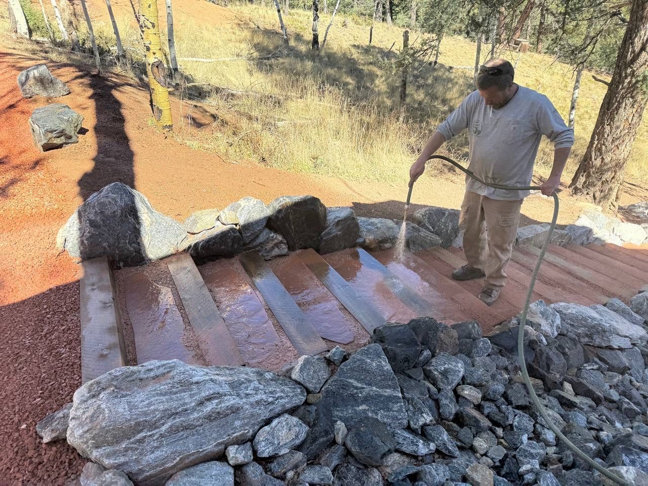 Man standing on a red roof, inspecting loose stones beside a pile of rocks on a hillside.