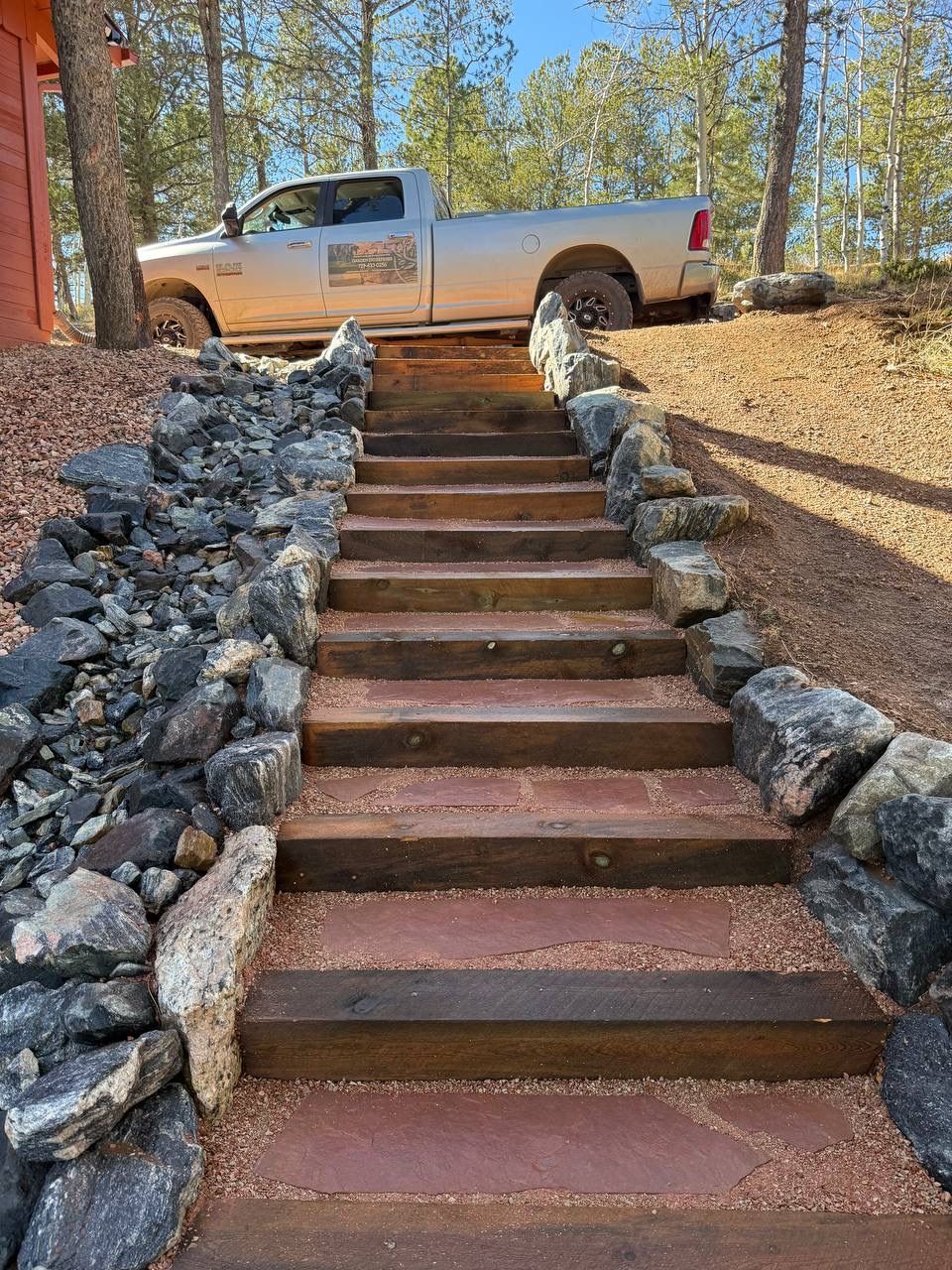 Stairway with stone borders leading up a dirt hill to a parked pickup truck in a wooded area