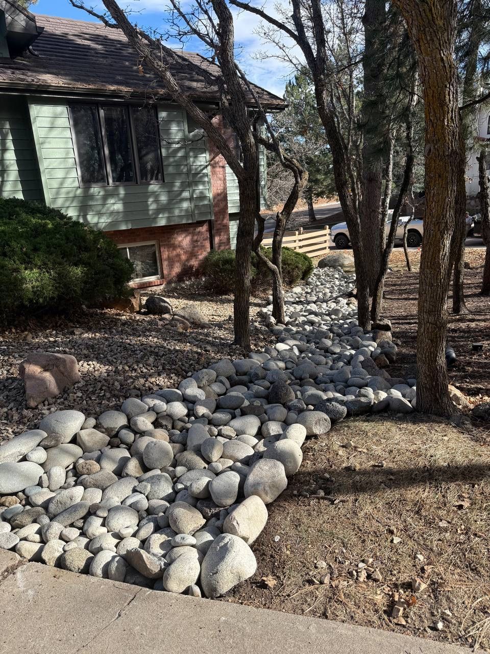 Rock-lined dry creek bed beside a house and trees in a yard