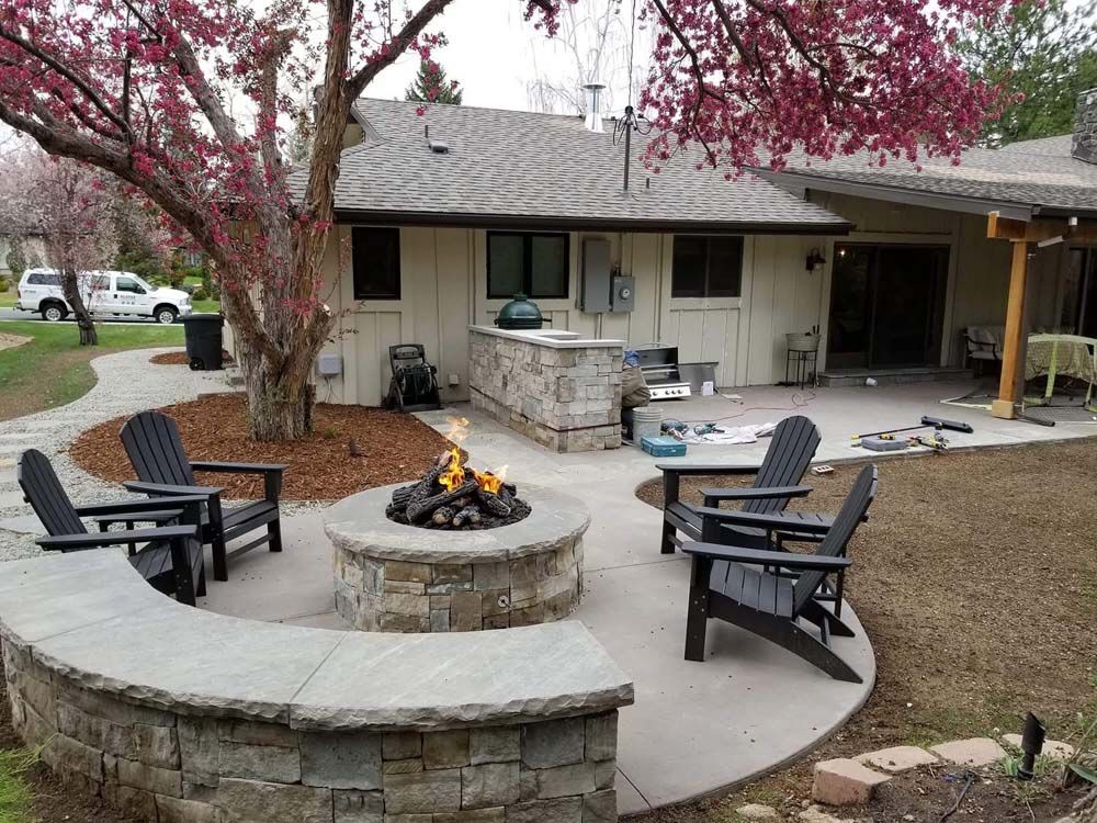 Backyard patio with fire pit, seating, stone wall, and flowering tree.