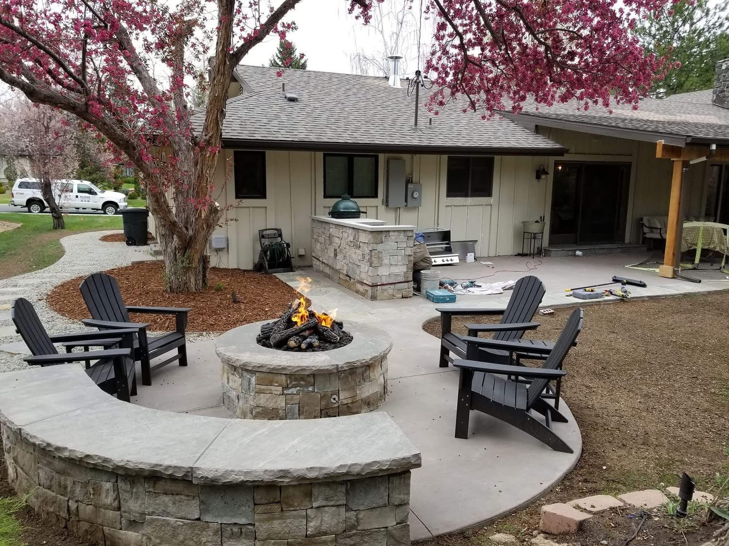 Backyard patio with stone fire pit, curved bench seating, and Adirondack chairs beside a house