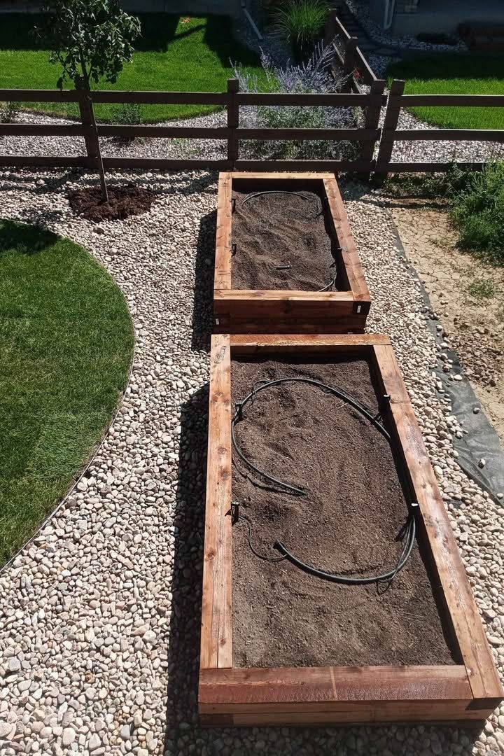 Two raised wooden garden beds, one filled with soil, beside a gravel path and fence.