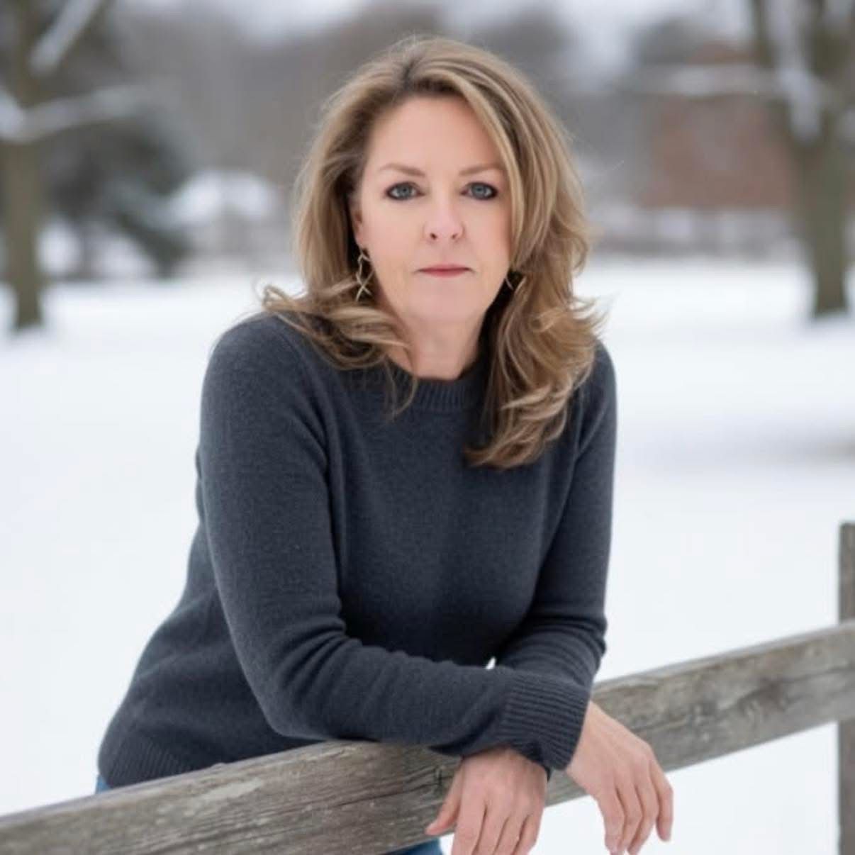 A woman in a gray sweater is smiling for the camera.