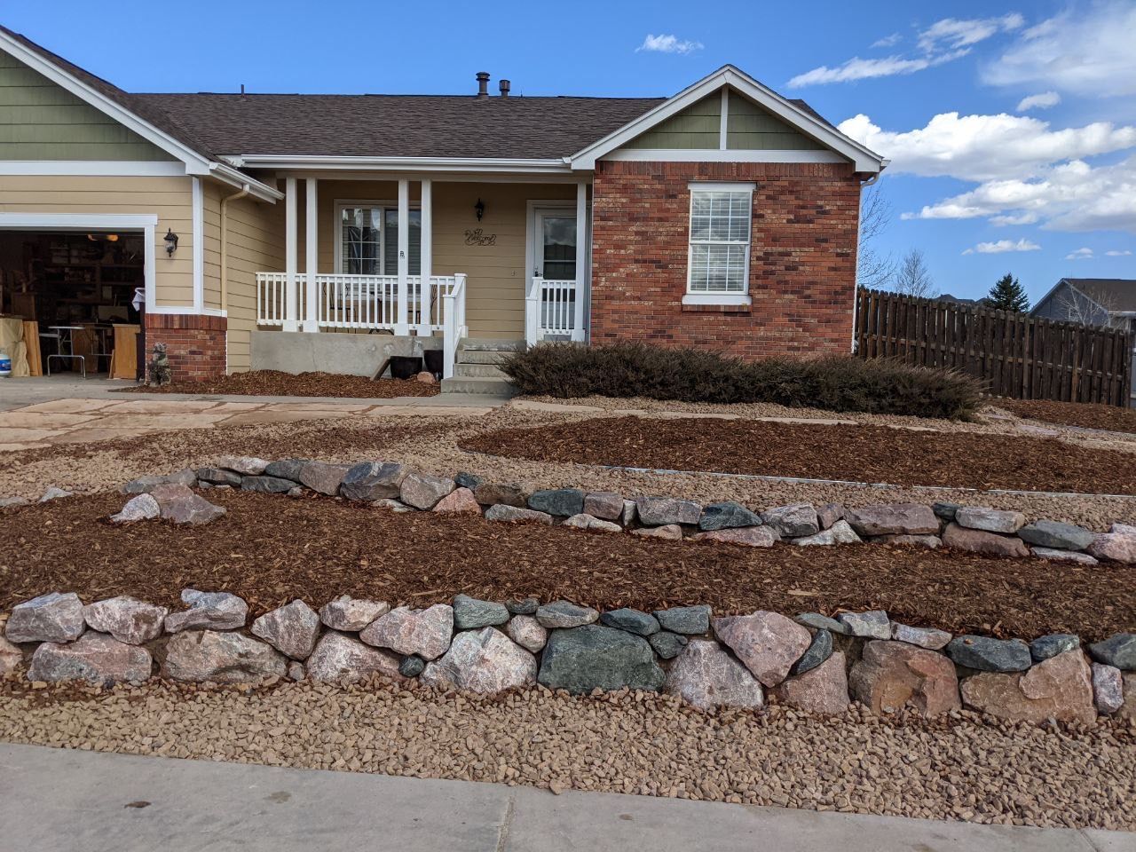 Single-story brick house with a front porch and landscaped rock garden under a blue sky