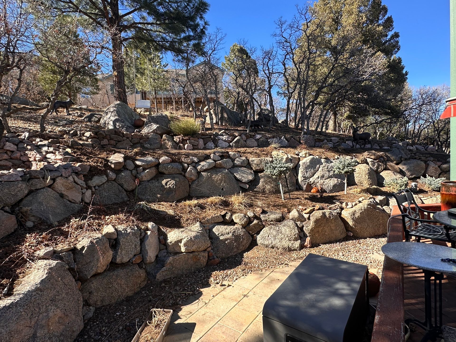 Stone terraced outdoor patio with trees, a blue sky, and a table and chair at the right edge
