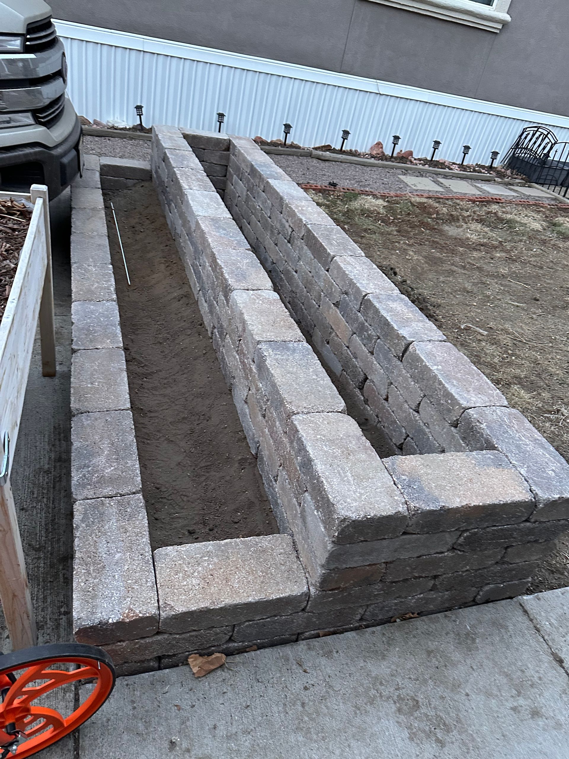 Two long rectangular stone planters with soil, beside a sidewalk and curb outdoors.