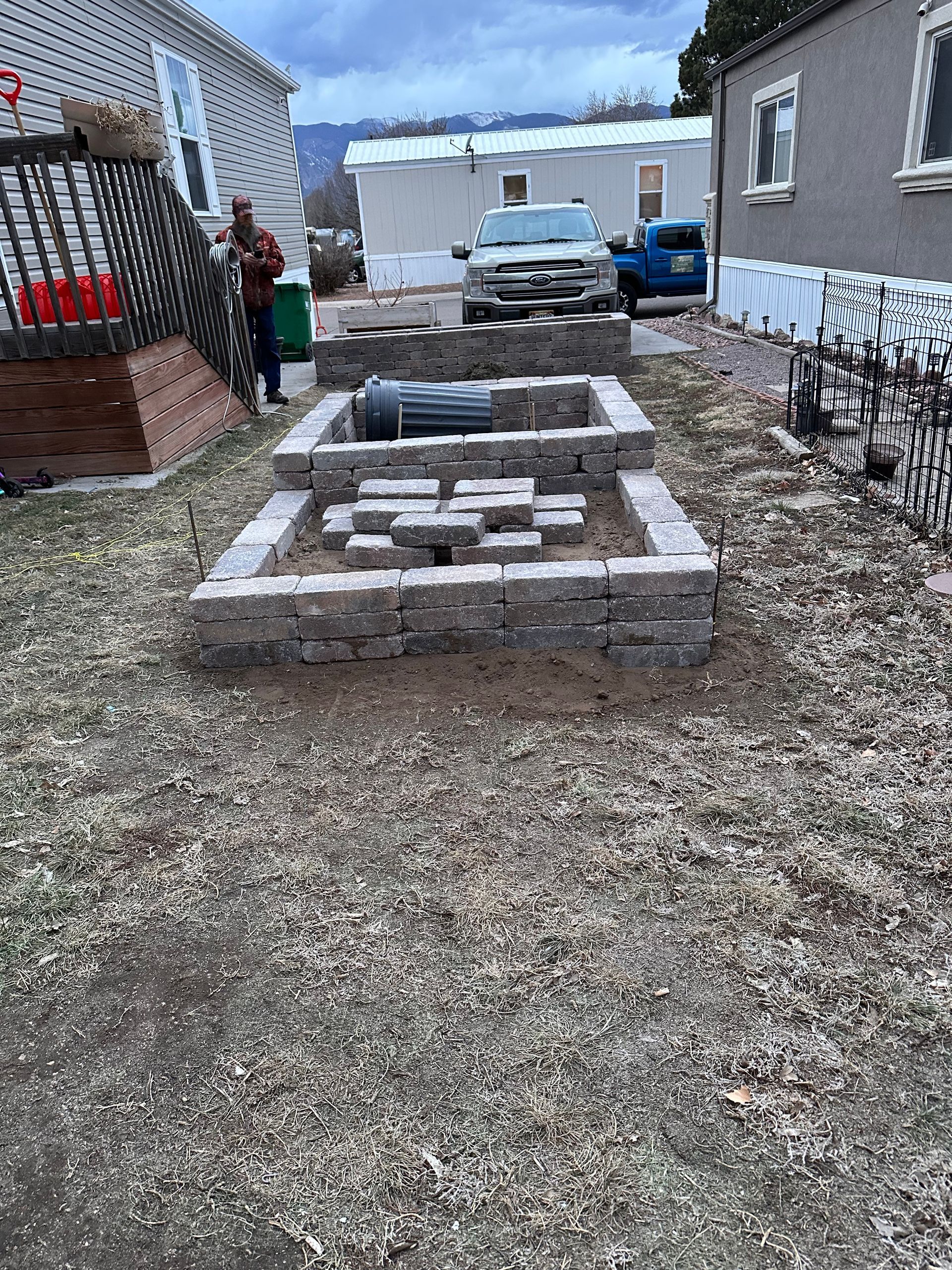 Backyard with raised stone garden bed and gravel path between houses, with white van and blue vehicle in the background