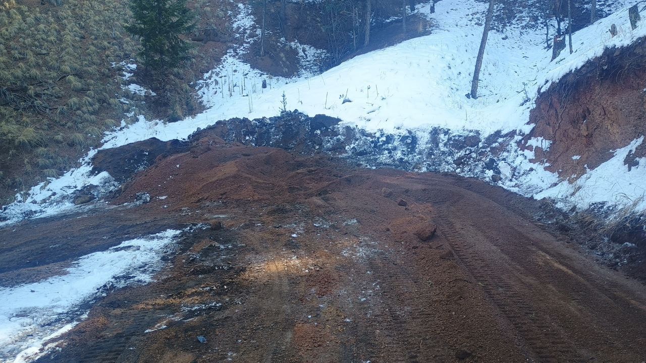 Snowy mountain road with muddy, brown landslide debris blocking the path
