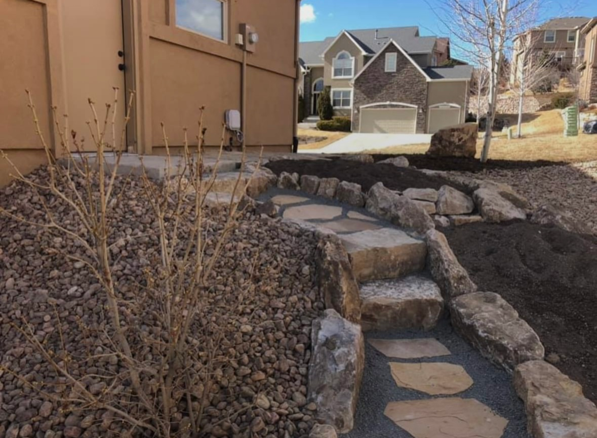 Stepping-stone path beside a tan house and rock garden in a suburban yard