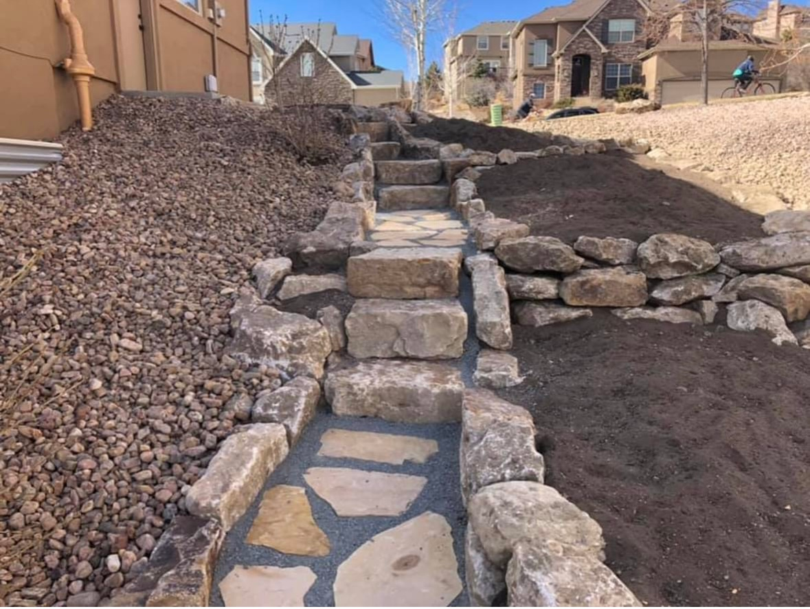 Stone steps and a flagstone path climb a landscaped dirt hillside between houses.