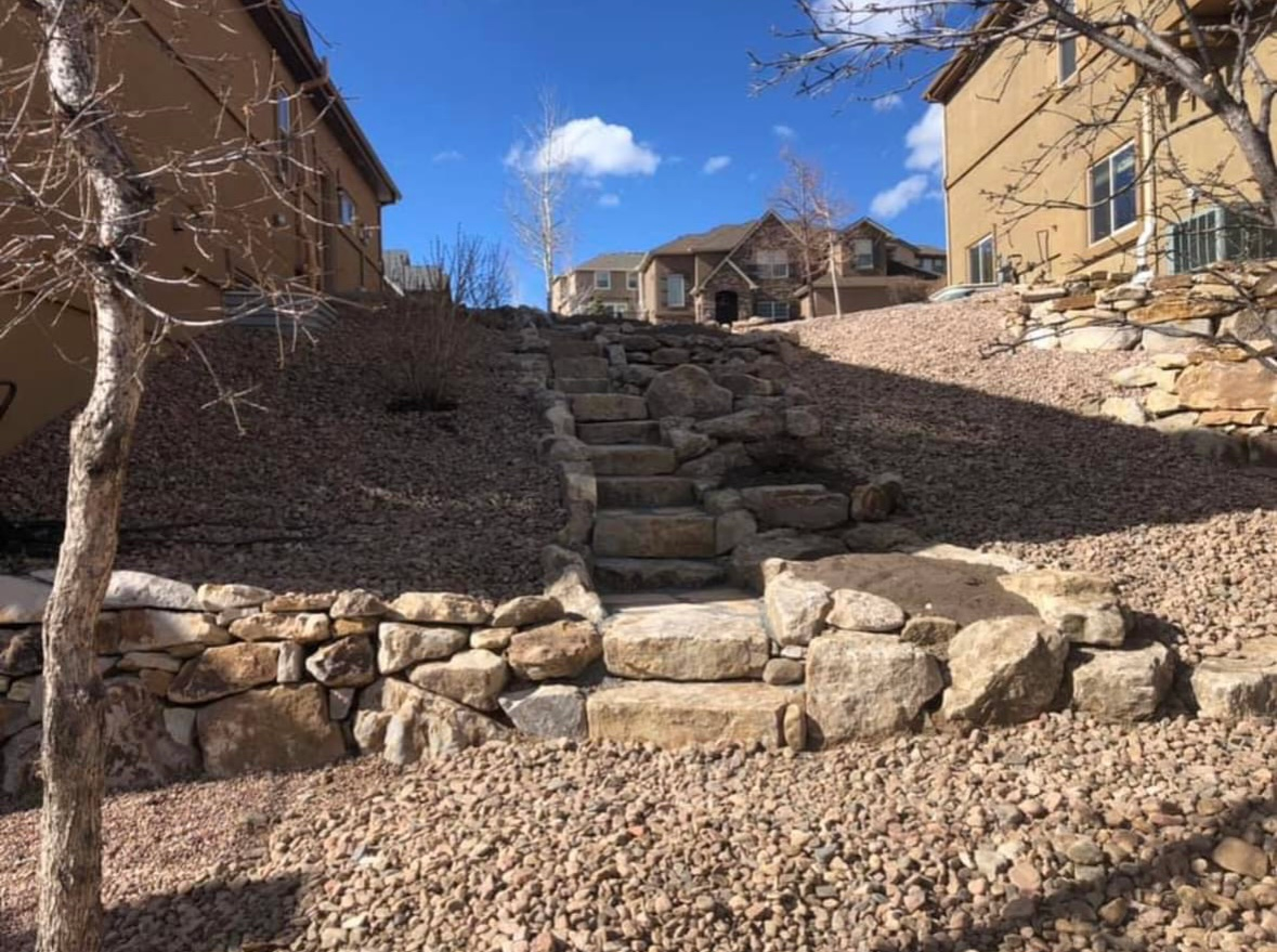 Rock steps ascending between tan houses in a sunny residential hillside area