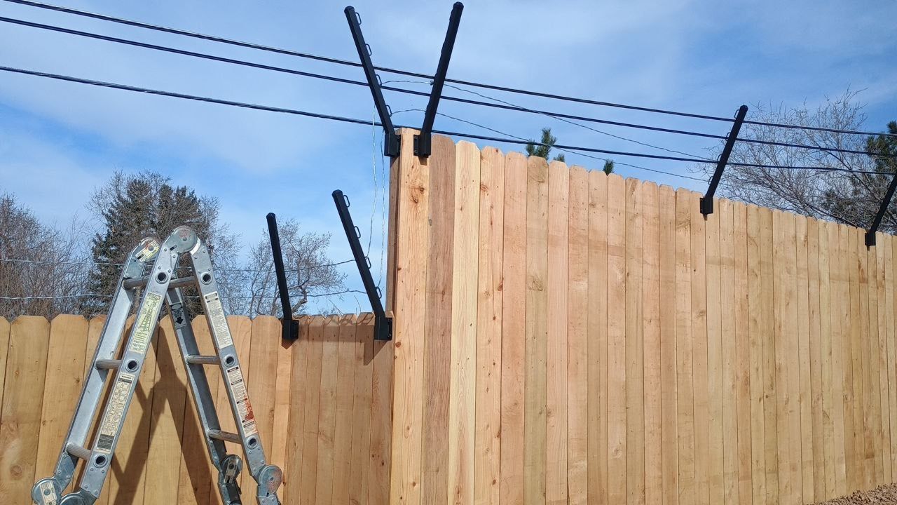Ladder beside a wooden fence topped with barbed wire under a clear blue sky