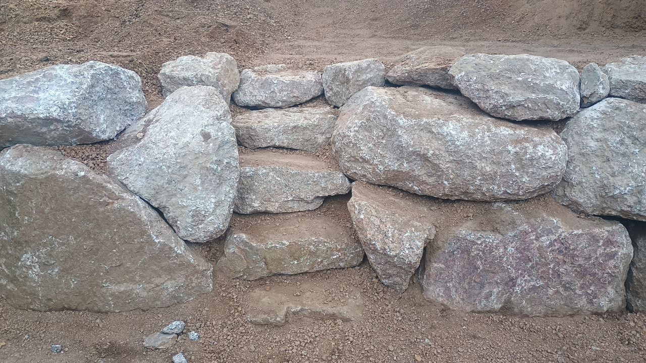 Stacked rough stones forming a low wall against sandy ground, with larger rocks on top and bottom