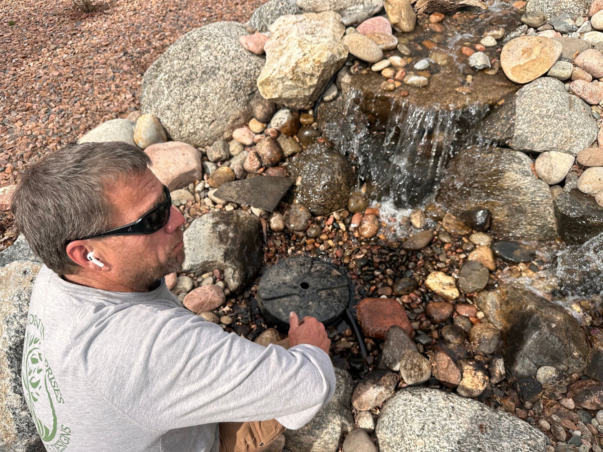 Man crouching by a rocky stream, looking at water flowing over stones