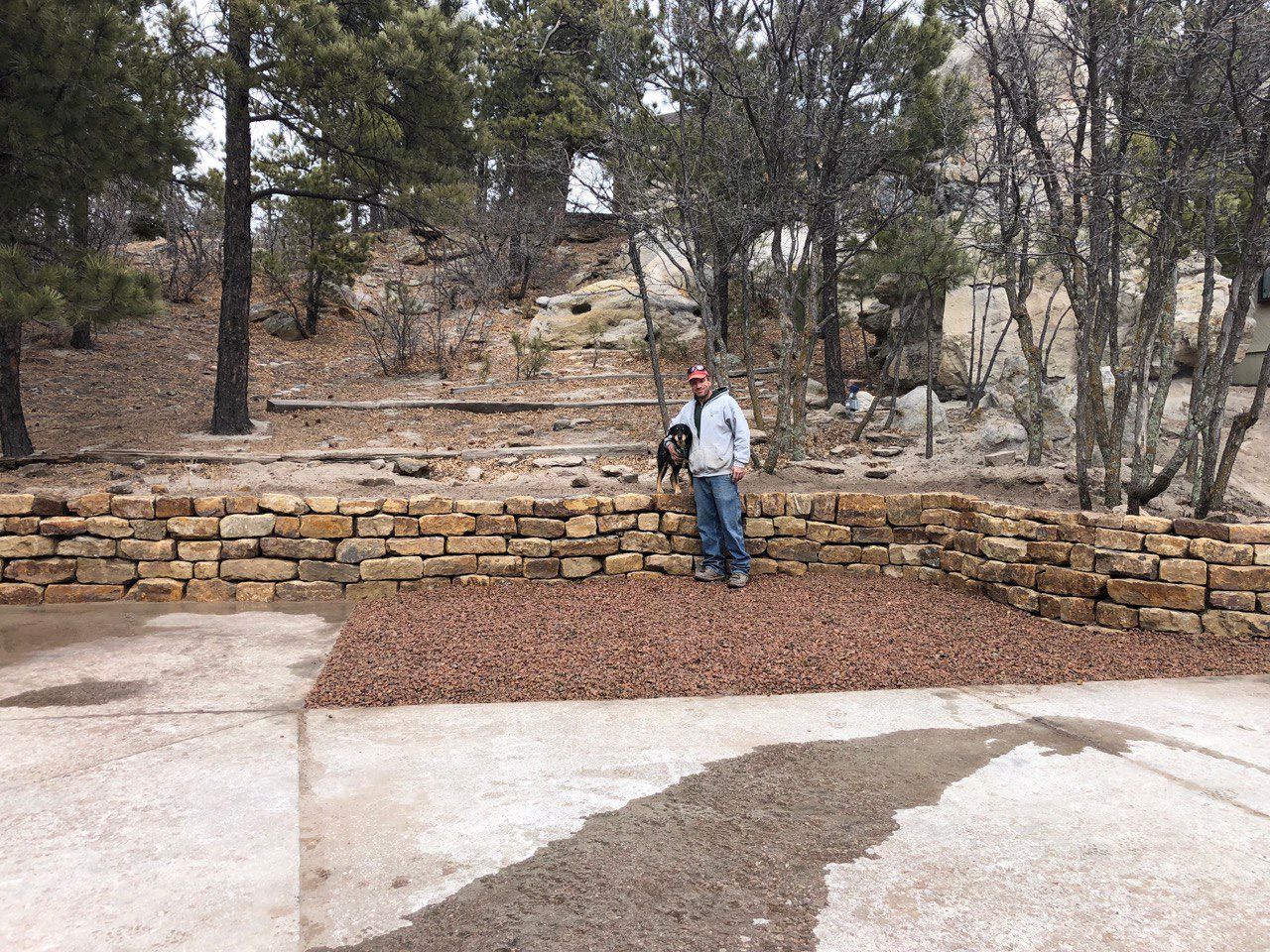 A man standing next to a stone wall with trees in the background