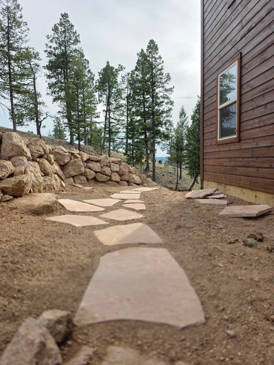 Stone path beside cabin leading through pine trees and a rocky yard.