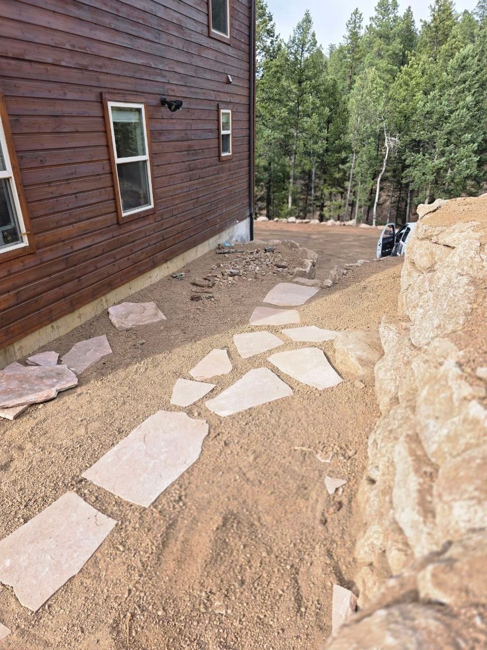 Stone path beside brown house leading to a wooded yard and rock wall