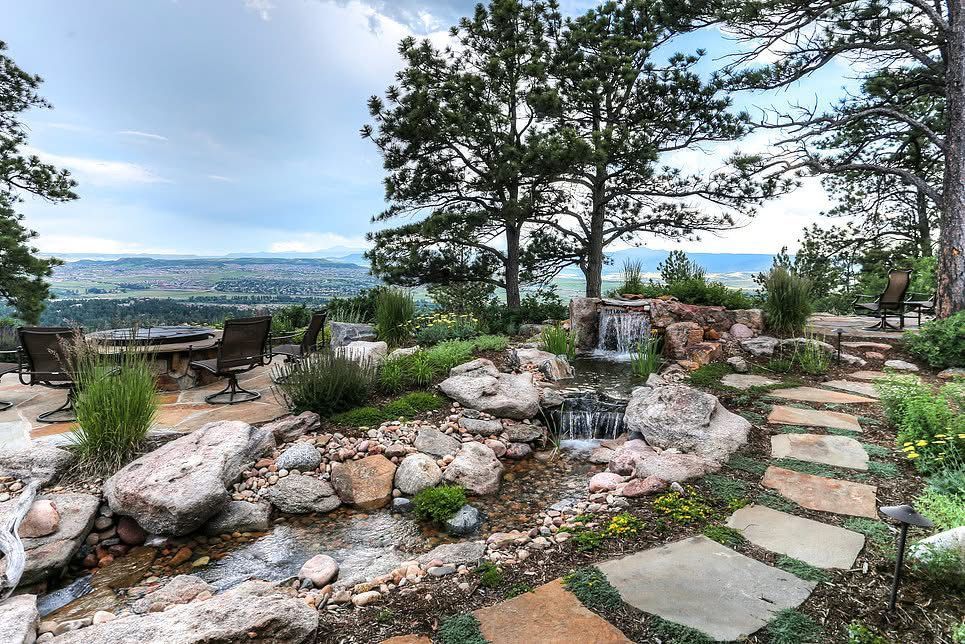 Rock garden patio with stepping stones, trees, and distant city views under a cloudy sky