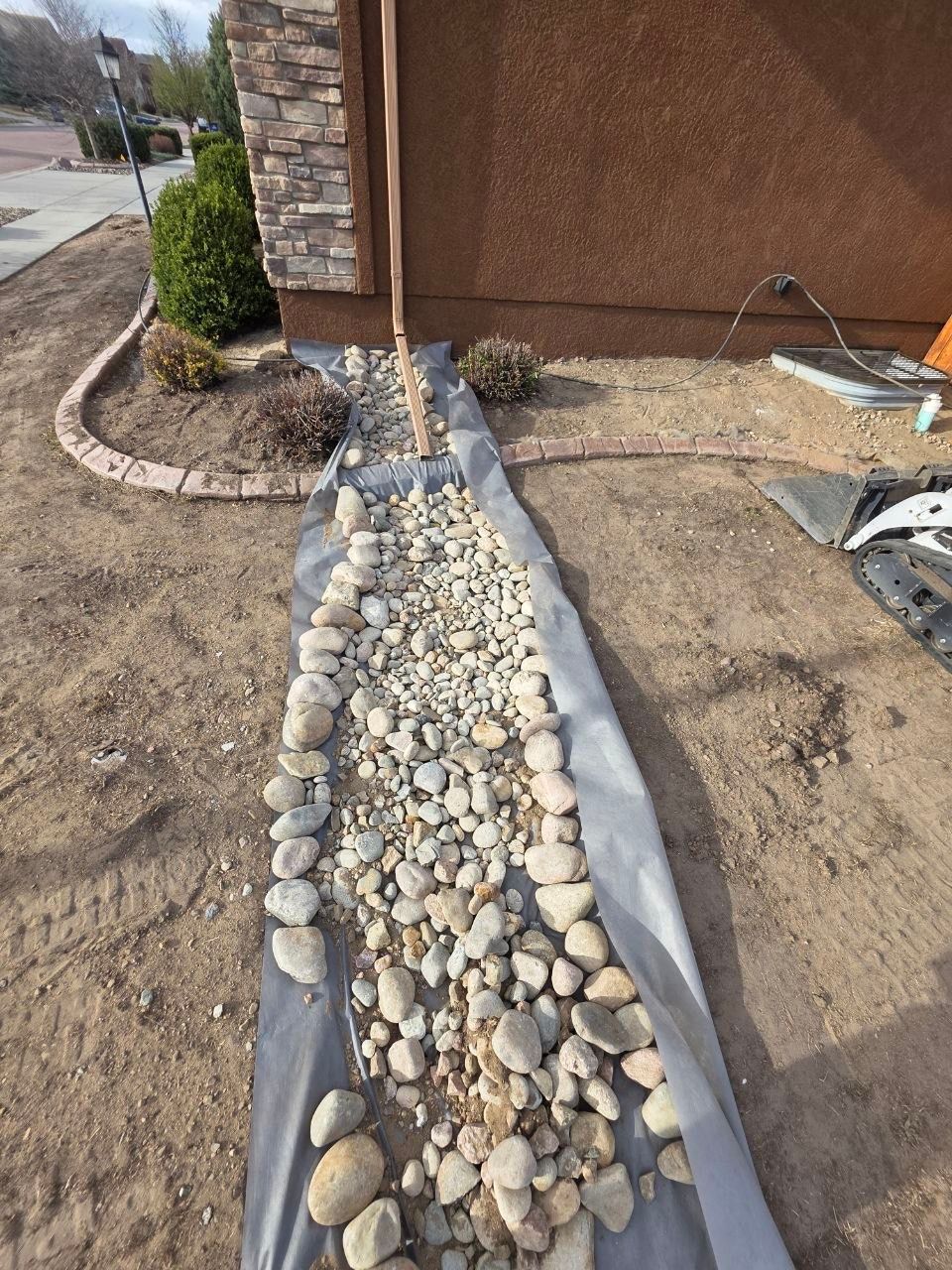 Rock-bordered drainage trench filled with white pebbles beside a stucco house wall