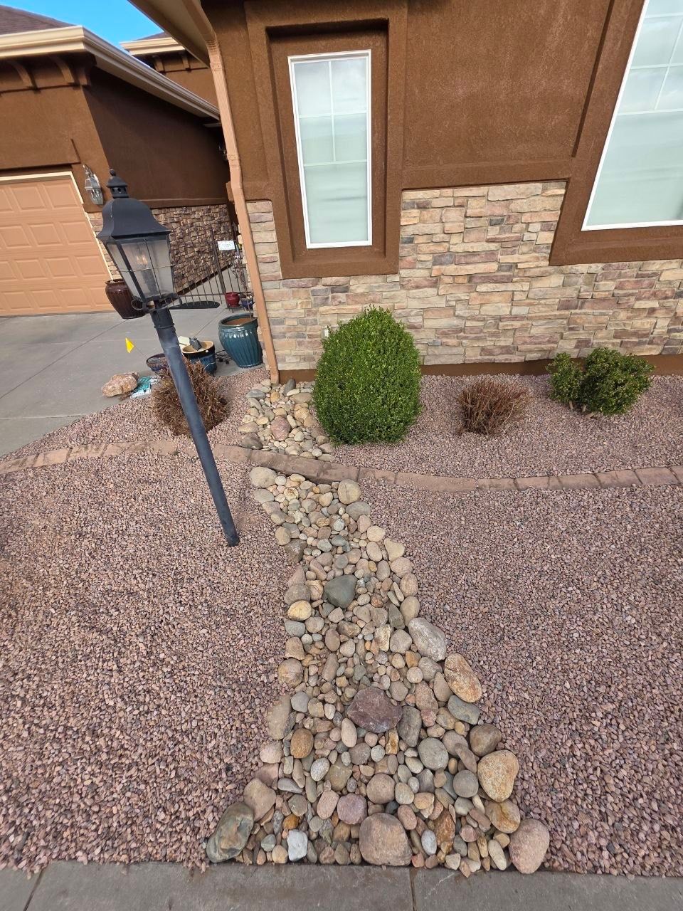 Desert-style front yard with gravel, stepping stones, shrubs, and a lantern by a stucco-and-stone house.