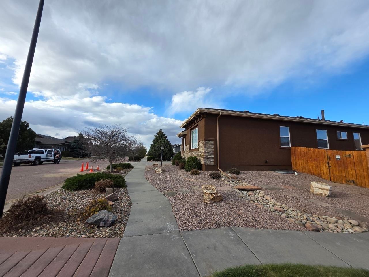 Residential sidewalk and desert landscaping beside a brown house under a cloudy sky