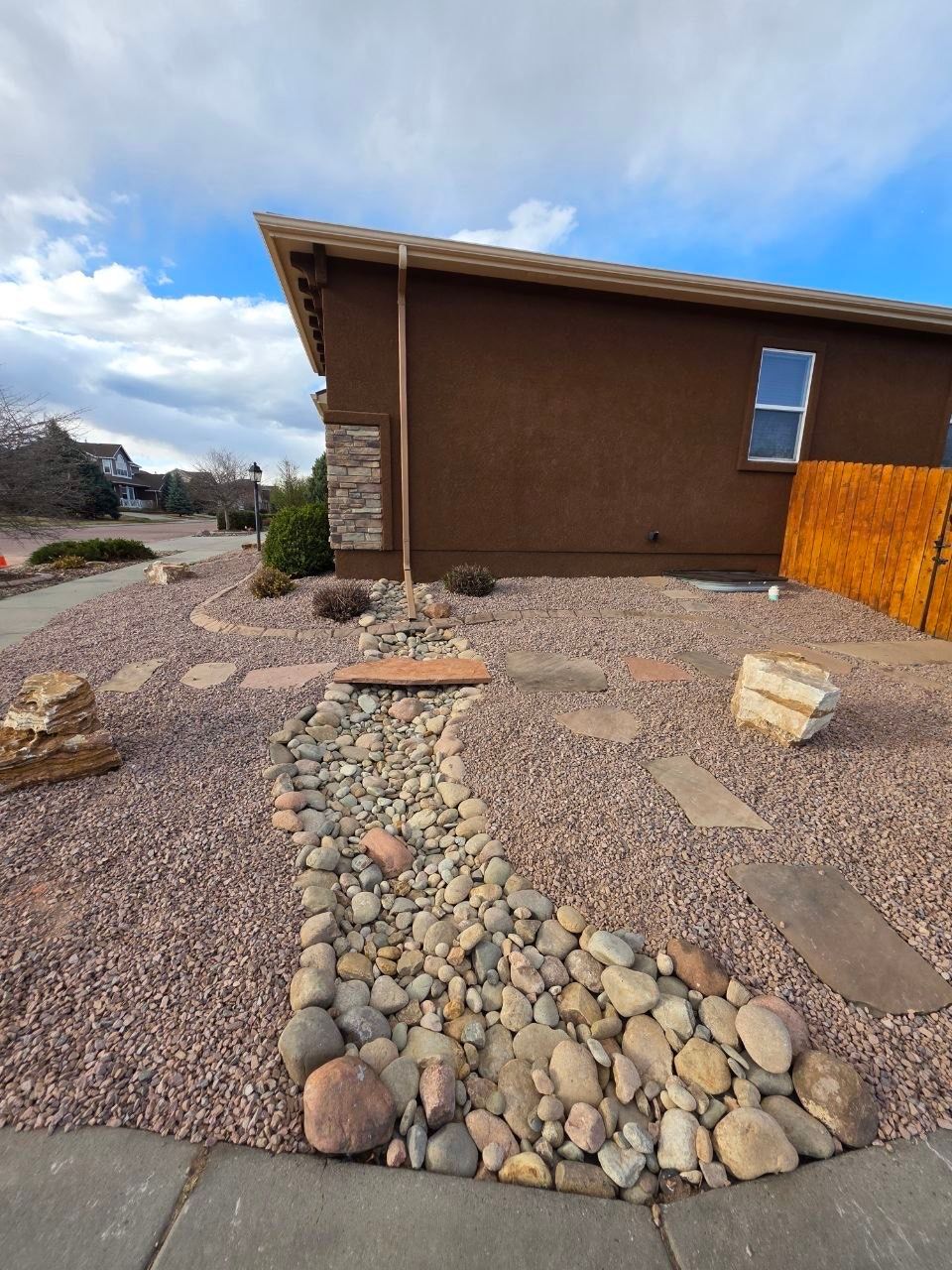 Rock landscape leading to a brown house with a blue sky overhead.