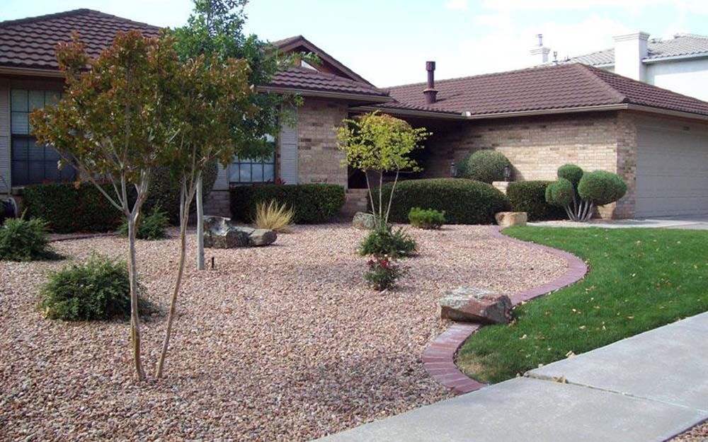 House exterior with a gravel yard, small trees, and a green lawn bordered by a brick edge.