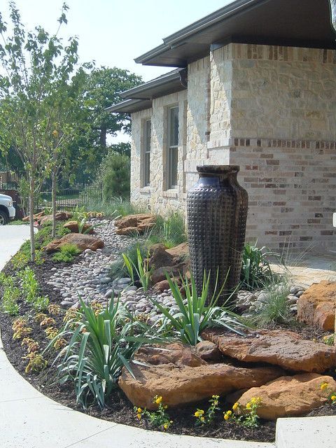 Landscaped front yard with a stone vase fountain beside a brick house and curved walkway