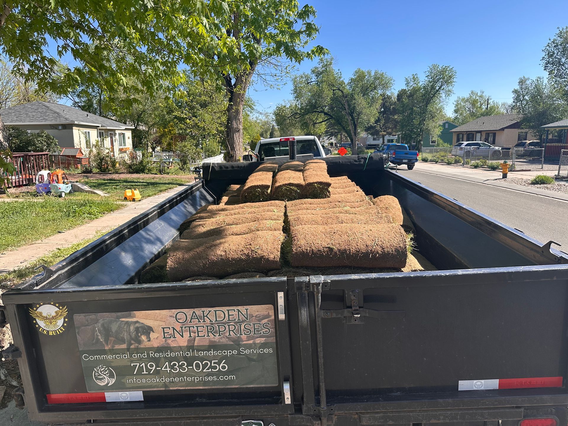 Black trailer loaded with hay bales parked on a sunny residential street