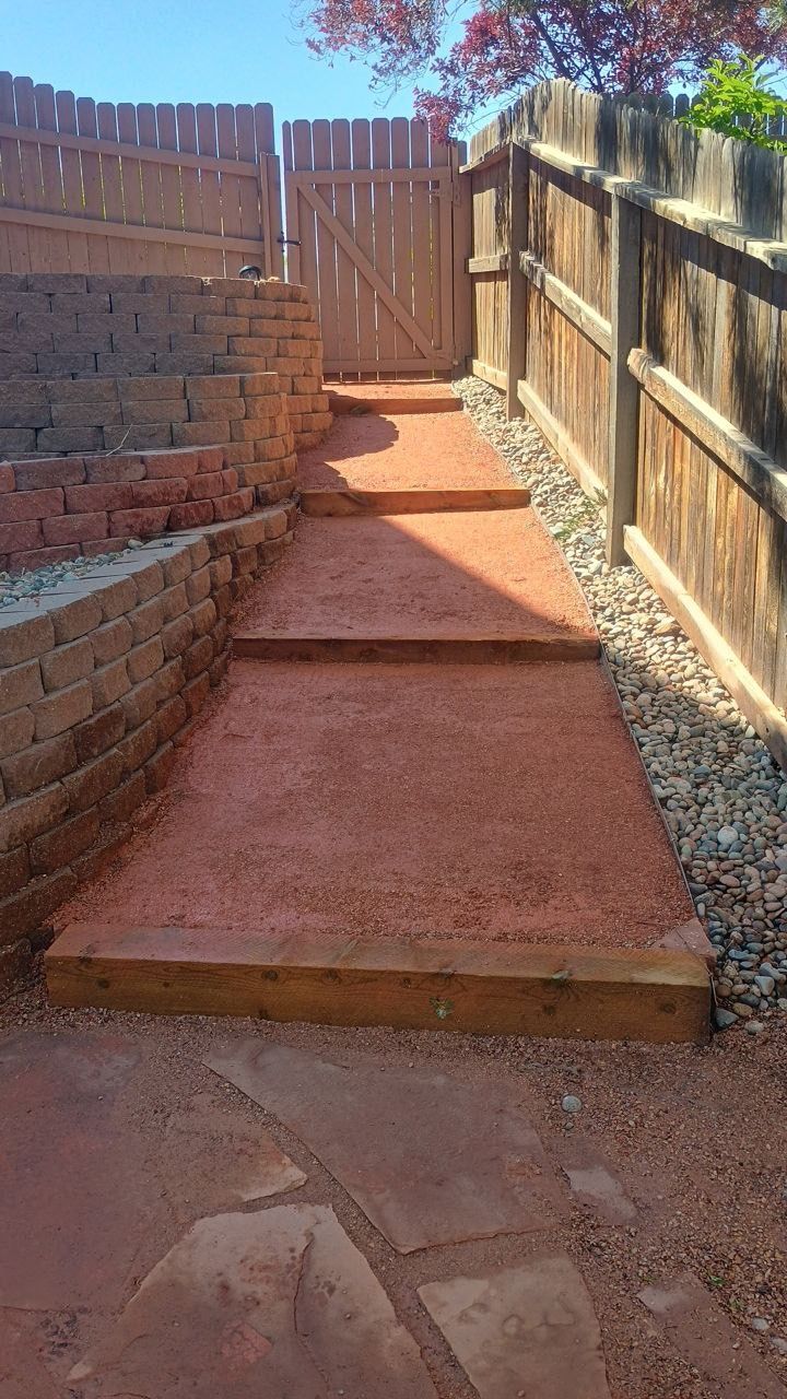 Narrow gravel path with a short wooden step leading to a fenced gate in a backyard.
