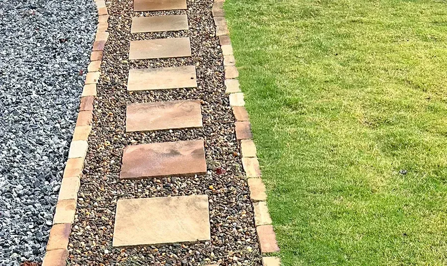 Stepping-stone path of square pavers through gravel beside a green lawn