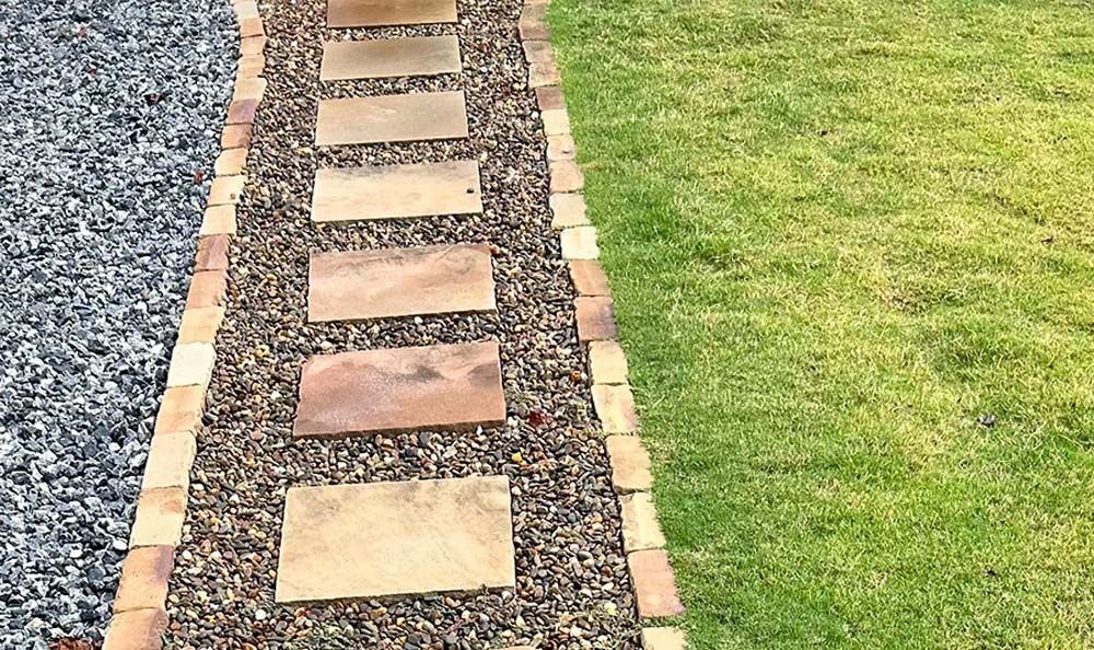 Stone pathway with gravel and brick borders, grass lawn on one side, and gray stone on the other.
