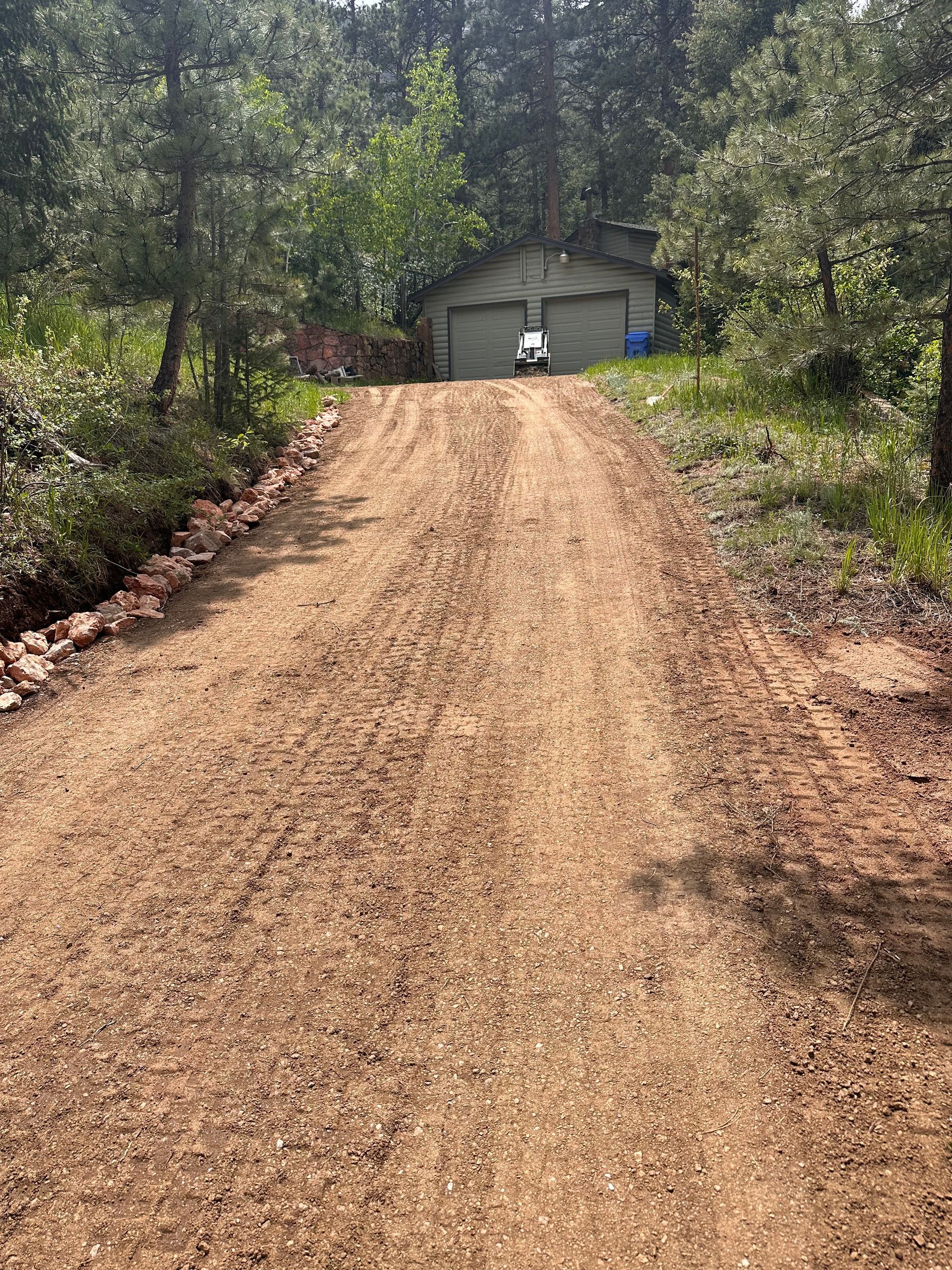 Gravel driveway leading to a small shed in a wooded yard, with a person standing near the entrance.