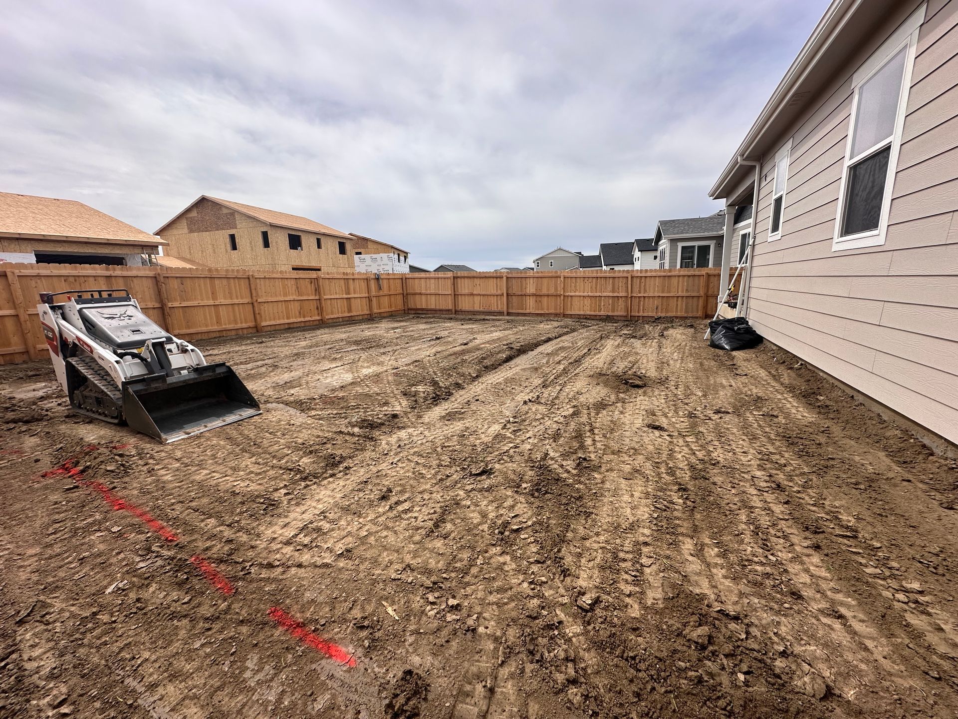 Backyard under construction with graded dirt, a small skid steer, and a house along the right side