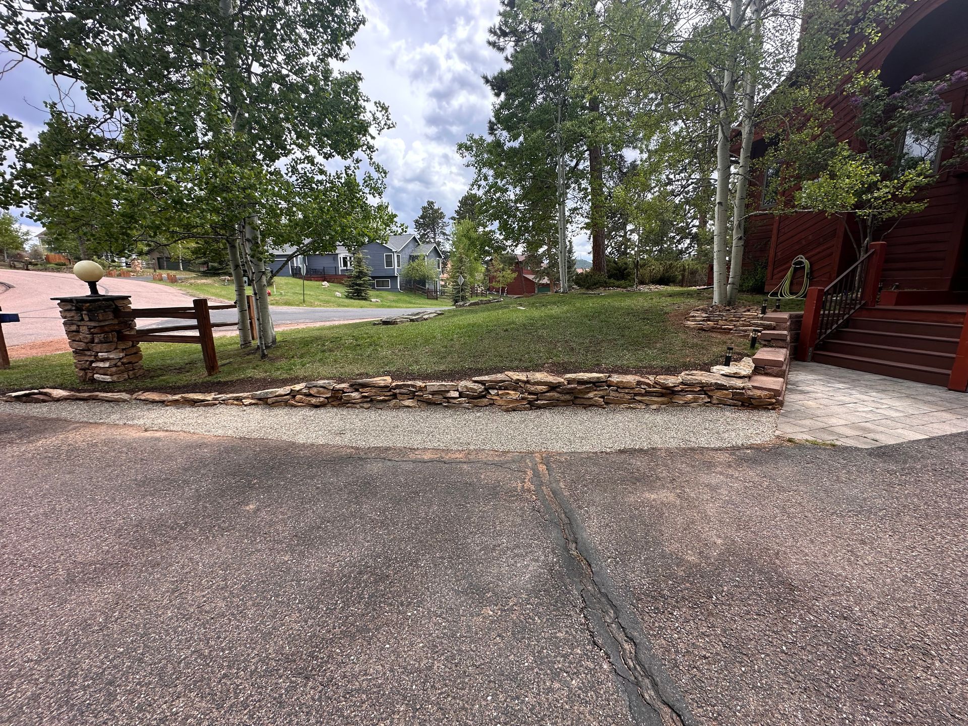Gravel driveway beside a stone planter and trees, with red stairs leading to a building on the right.