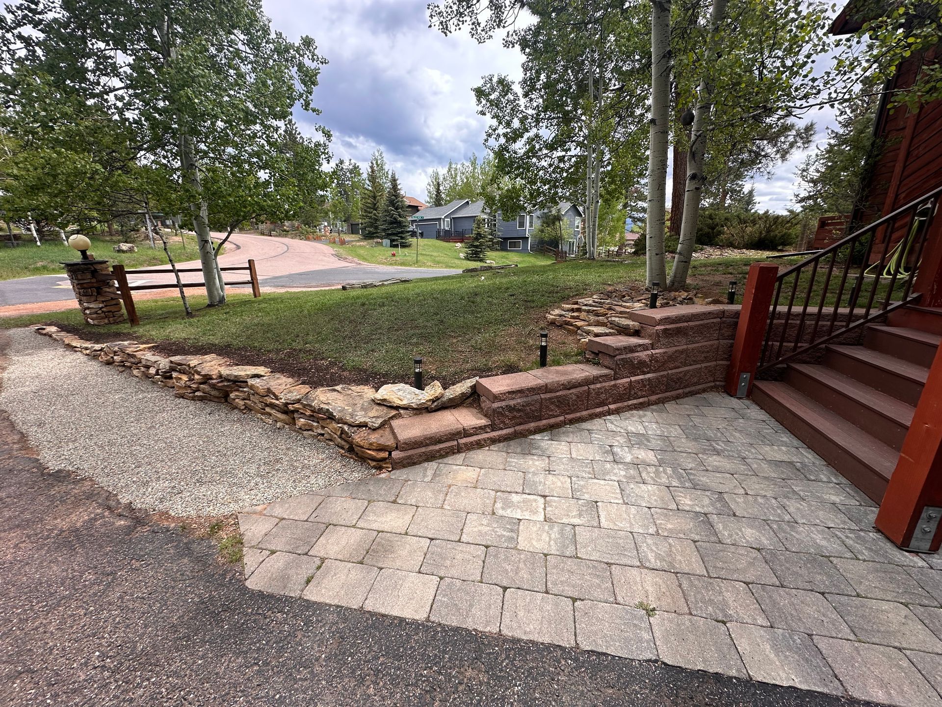 Stone patio and brick steps beside a landscaped yard with trees and a gravel path.