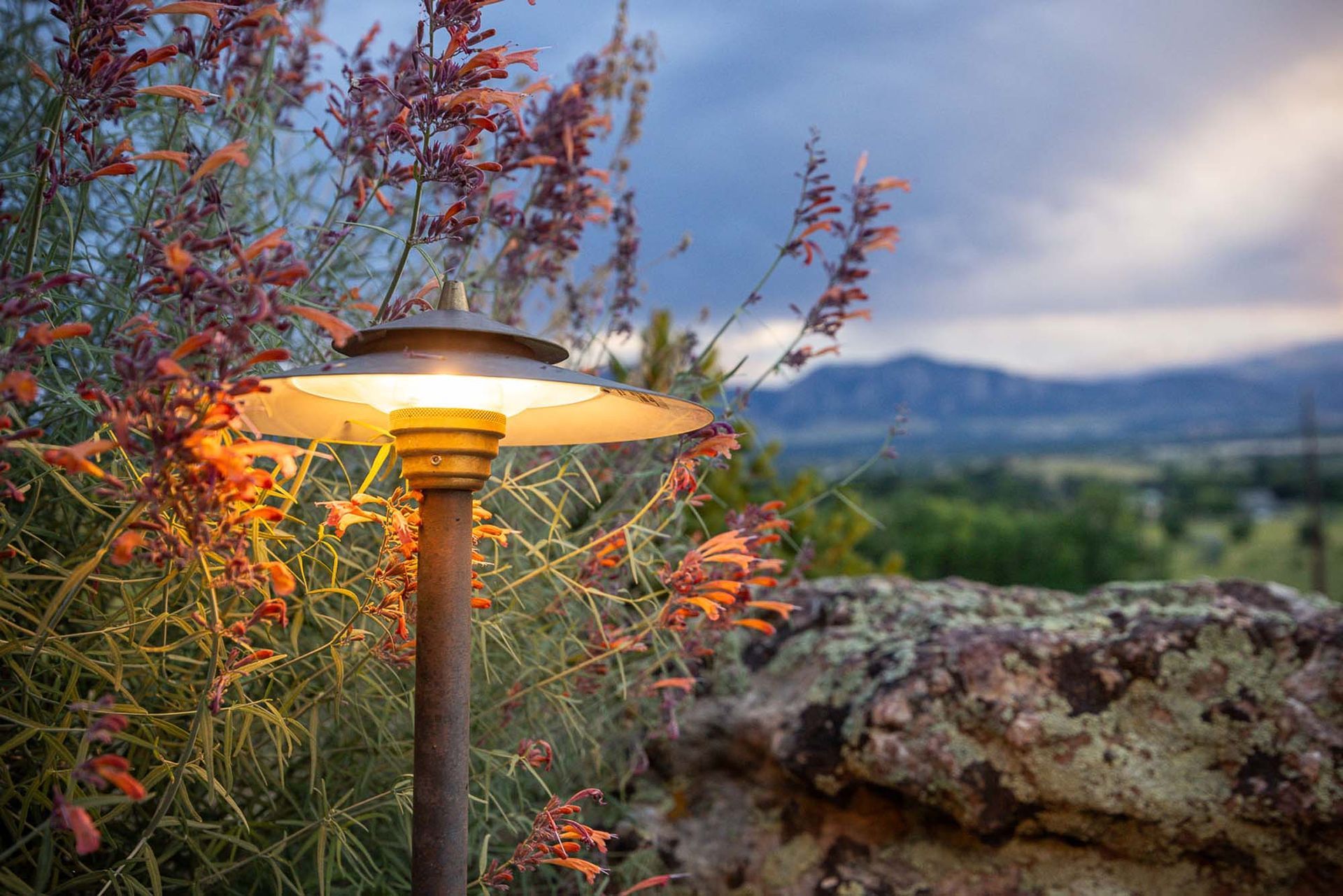 A lamp is lit up in a garden with mountains in the background