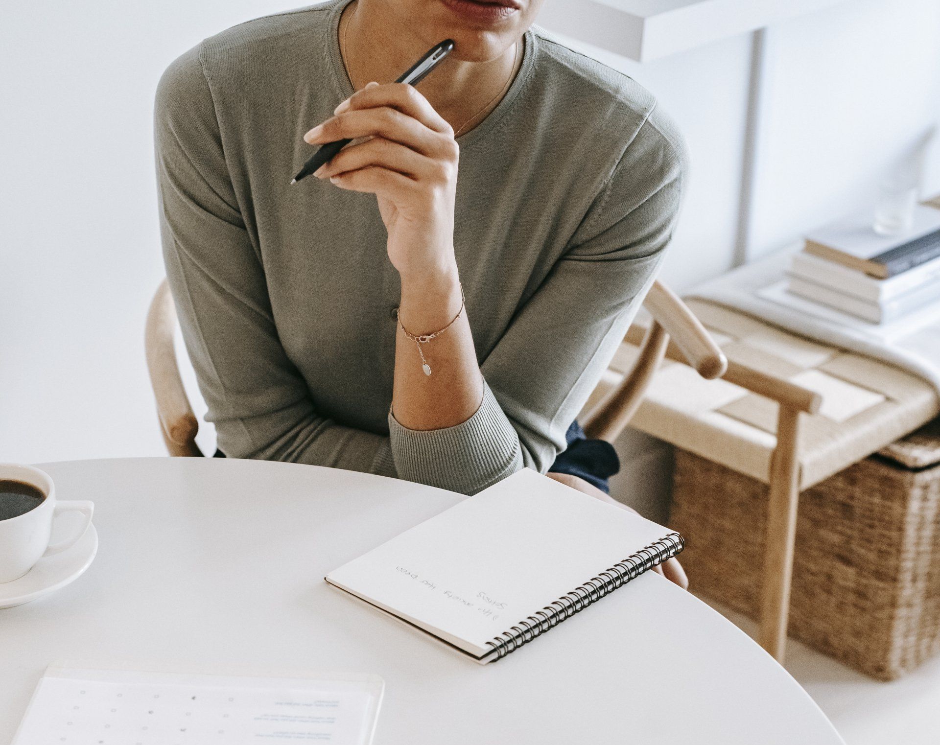 A woman is sitting at a table with a notebook and a pen in her hand.