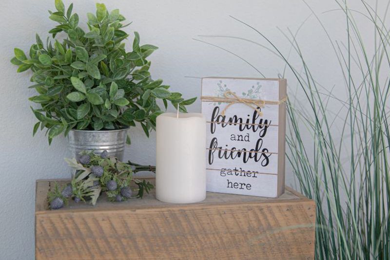 A wooden box with a sign that says `` family and friends gather here '' next to a plant and a candle.