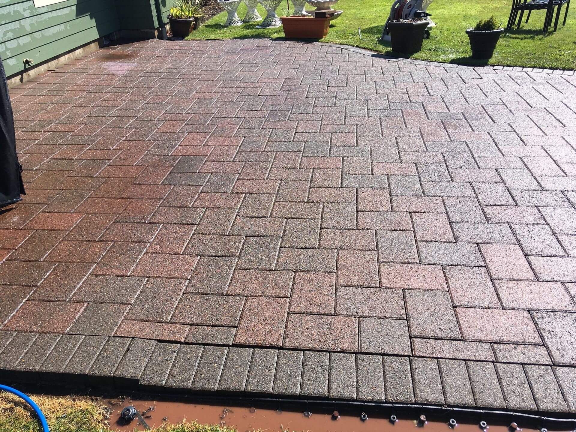 A brick patio being power washed; half is clean, half is dirty. Outdoors, daytime.