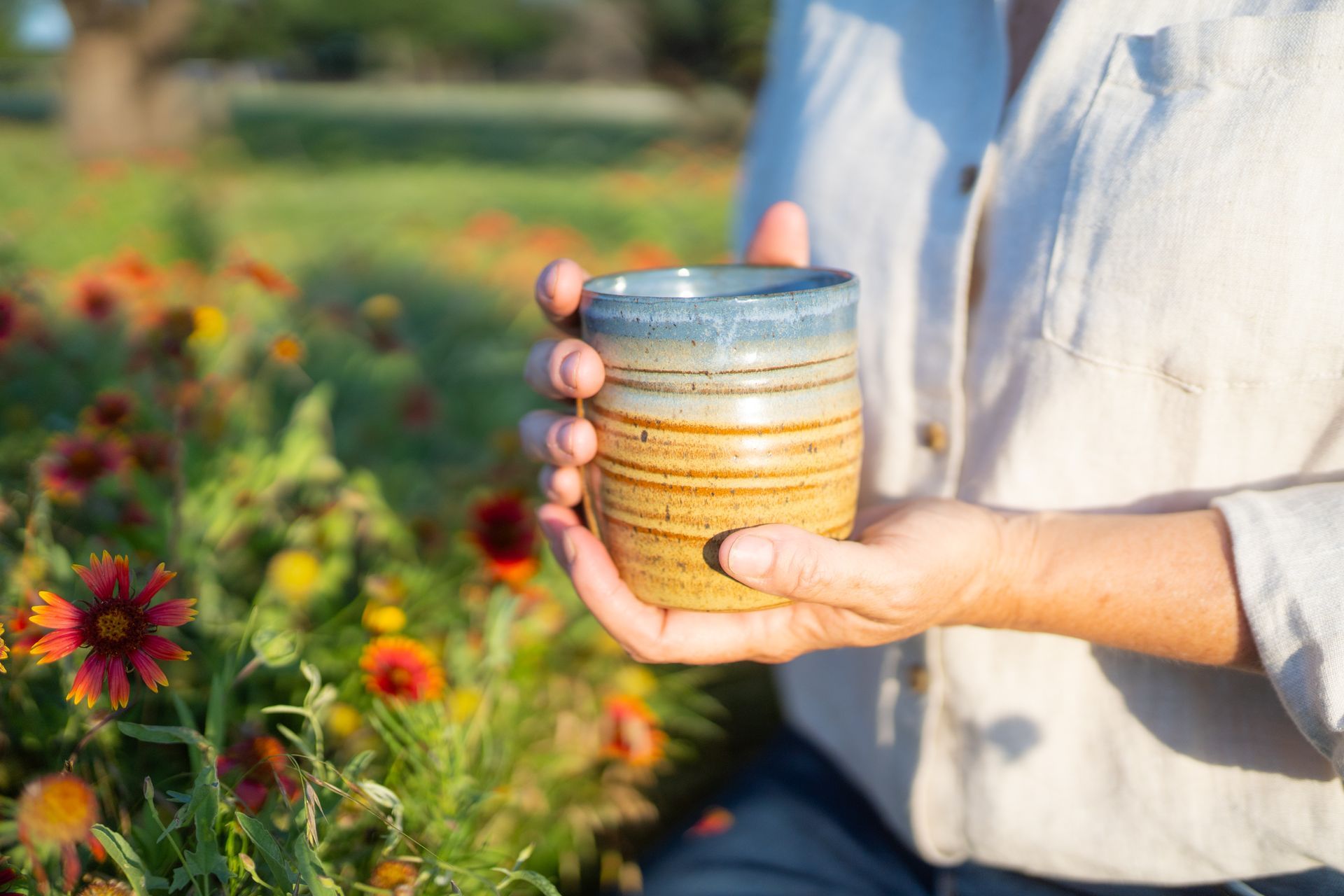 A person is holding a cup in their hands in front of a field of flowers.