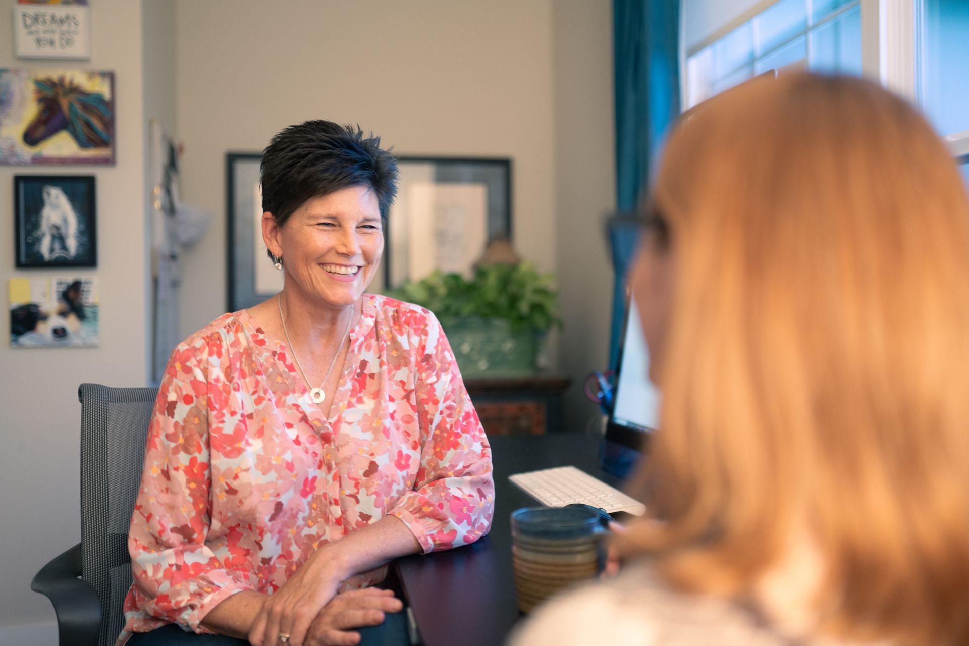 A woman is sitting at a desk talking to another woman.